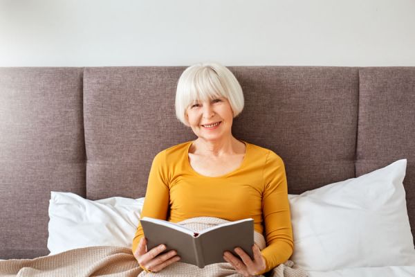 frau-mit-weissen-haaren-sitzt-in-einem-boxspringbett